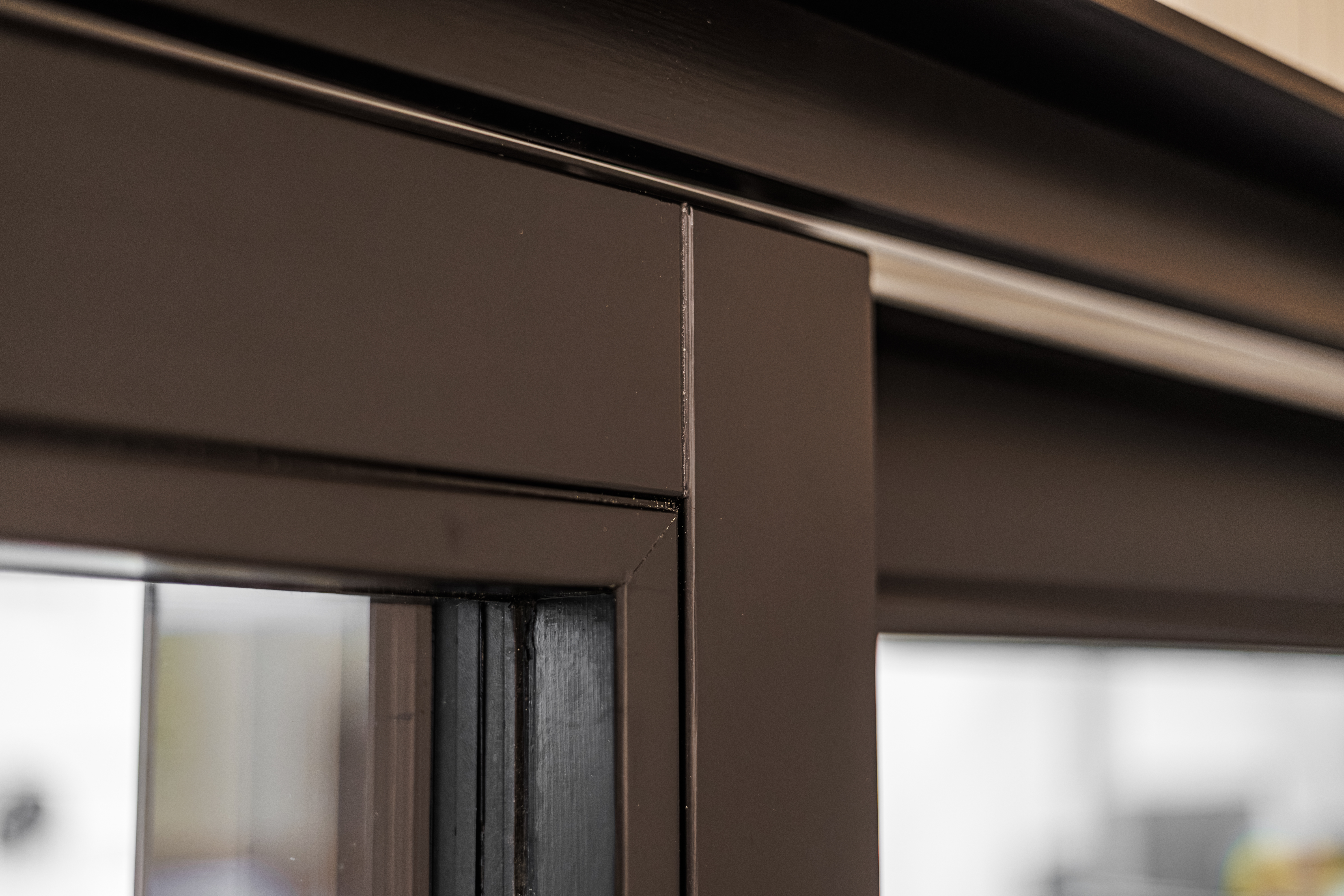Close-up of a brown aluminum sliding door frame corner with visible glass panel and track system, highlighting modern architectural design and precise construction details